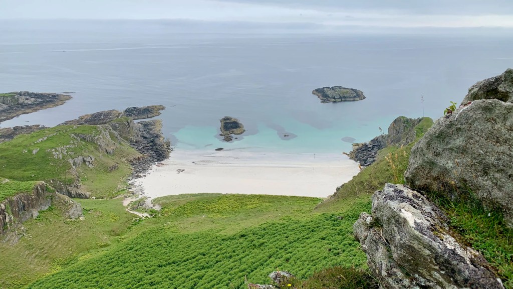 White sand beach on Mull, Scotland, with turquoise water and rocky cliffs under a cloudy sky.