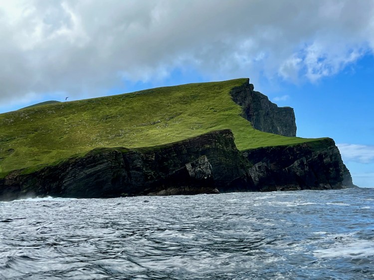 Foula island cliffs, Shetland. Green grassy top, dark rocky base. Wildlife habitat.