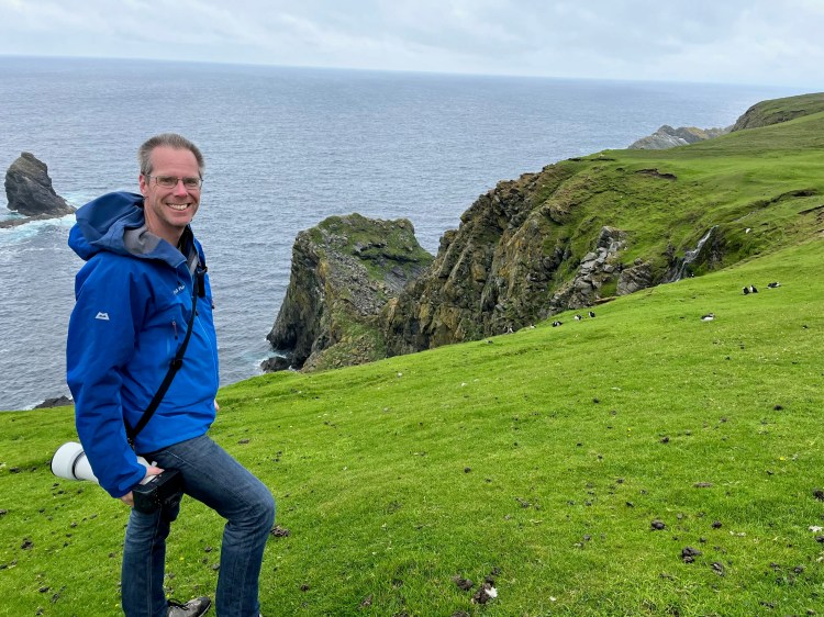 Photographer on Shetland's North Isles with rugged coastline and puffins.
