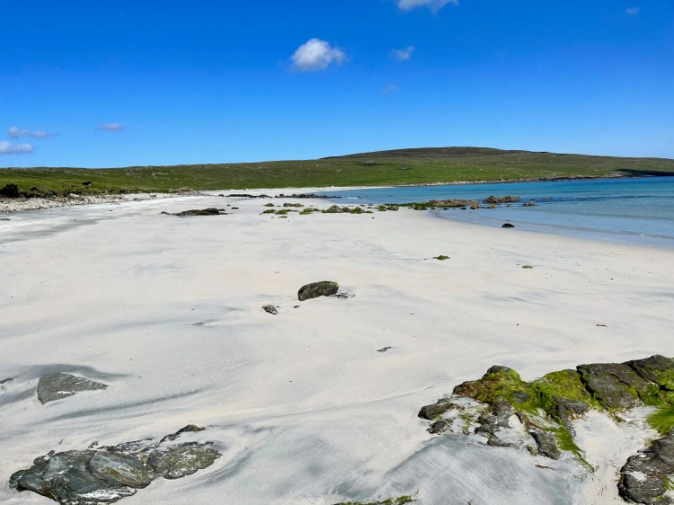 Shetland beach with white sand, rocks, and blue sky. North Isles landscape.