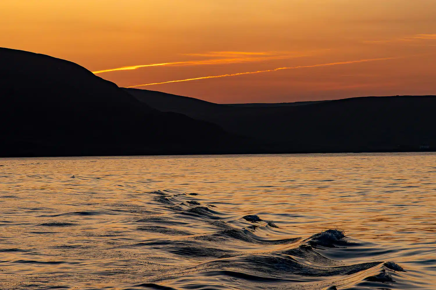 Sunset over water with gentle waves and silhouetted hills in Shetland. Mainland & Mousa landscape.