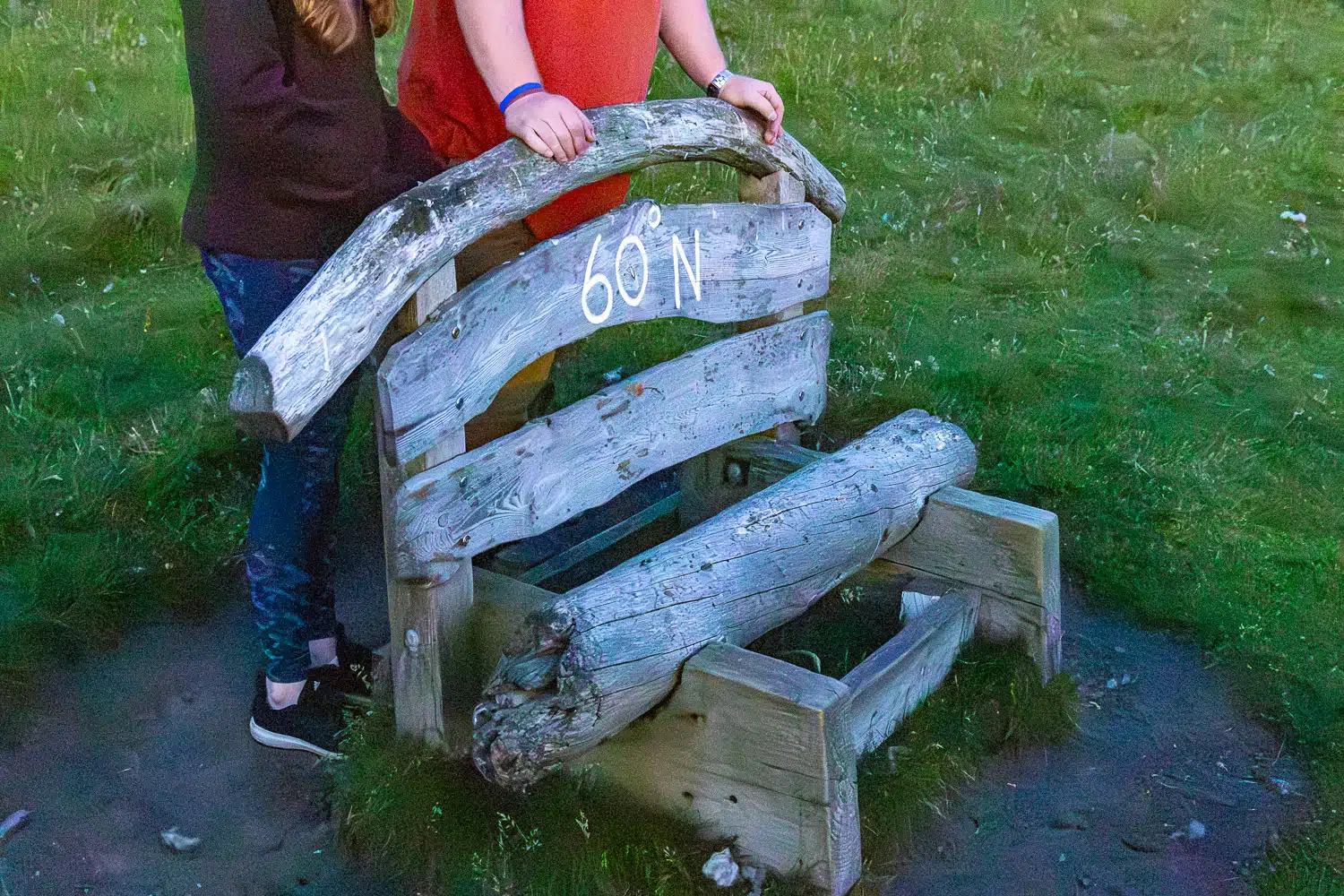 People stand by a wooden bench marked "60 N" in Shetland.