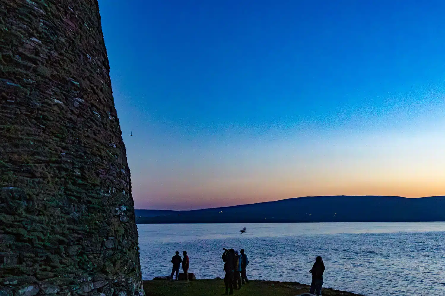 Shetland coastline view at dusk near Mousa Broch, with people watching seabirds.