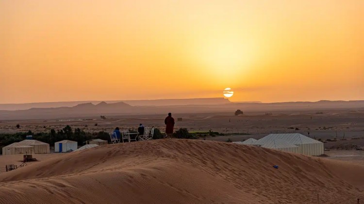 Sunset over Moroccan desert camp. People on dune enjoy the view.