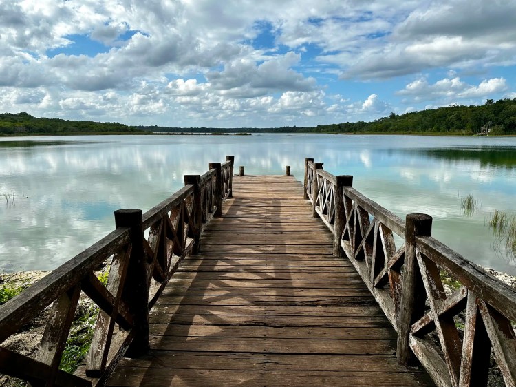 Wooden dock extending into a calm lagoon, reflecting the sky. Punta Laguna nearby.