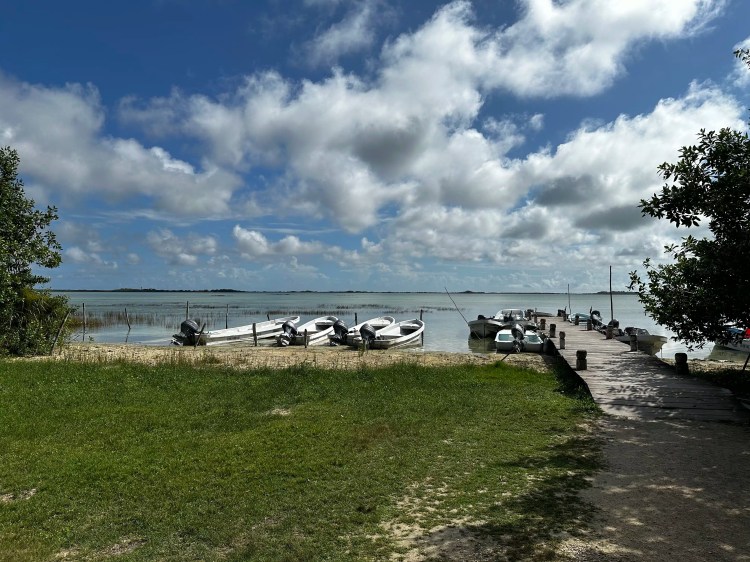Boats docked at Sian Ka'an lagoon, with a pier under a partly cloudy sky. Birding Muyil area.