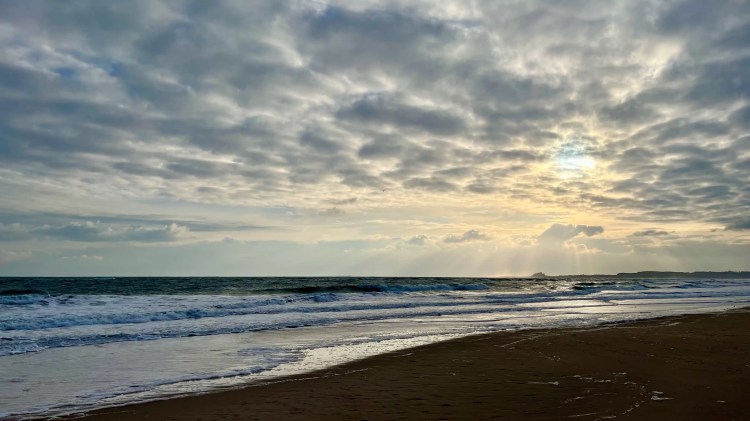 Northumbria coastline under a dramatic, cloudy sky with sun rays breaking through.